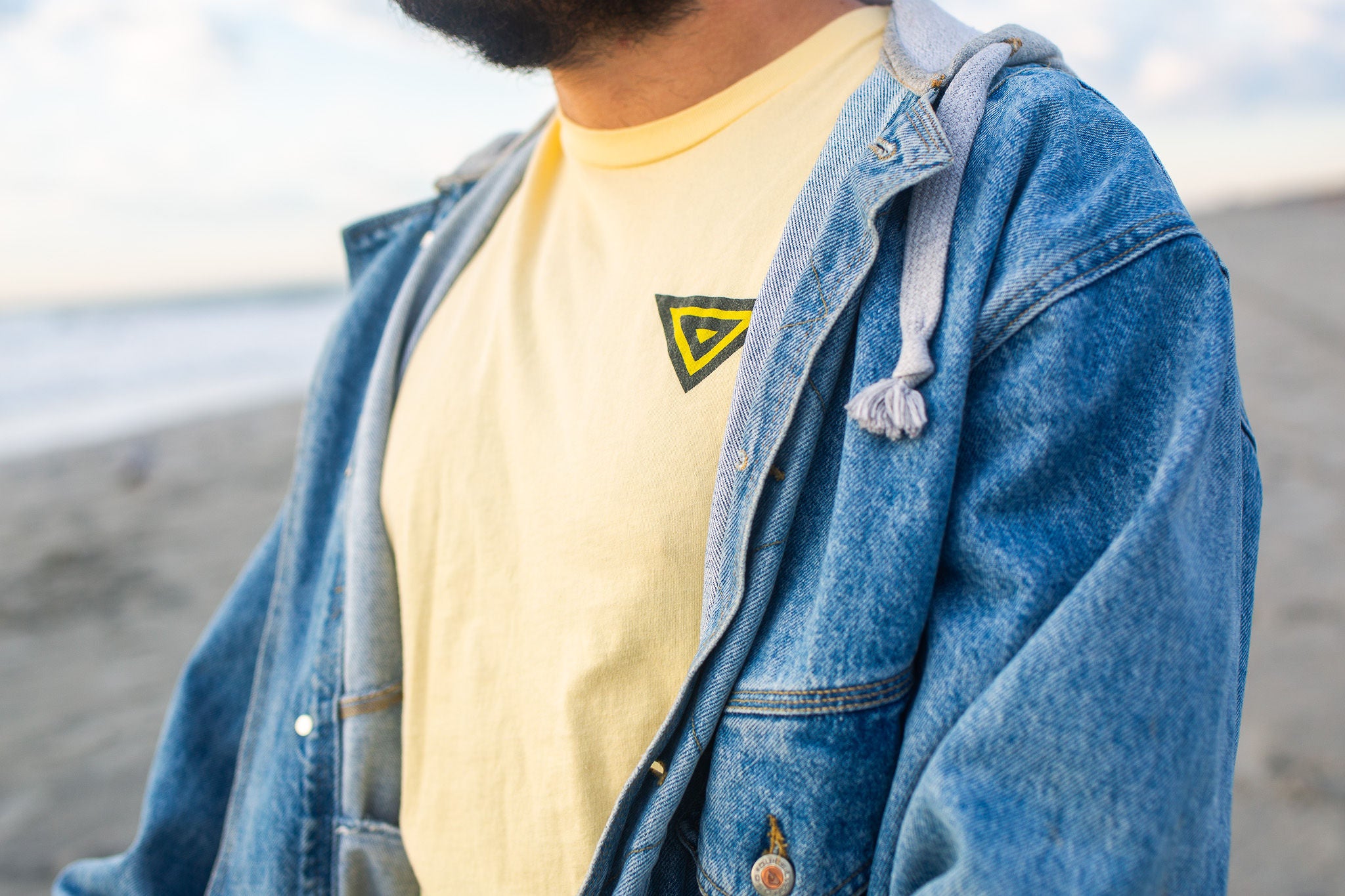 front facing man wearing yellow pandion logo tee shirt with a denim jacket
