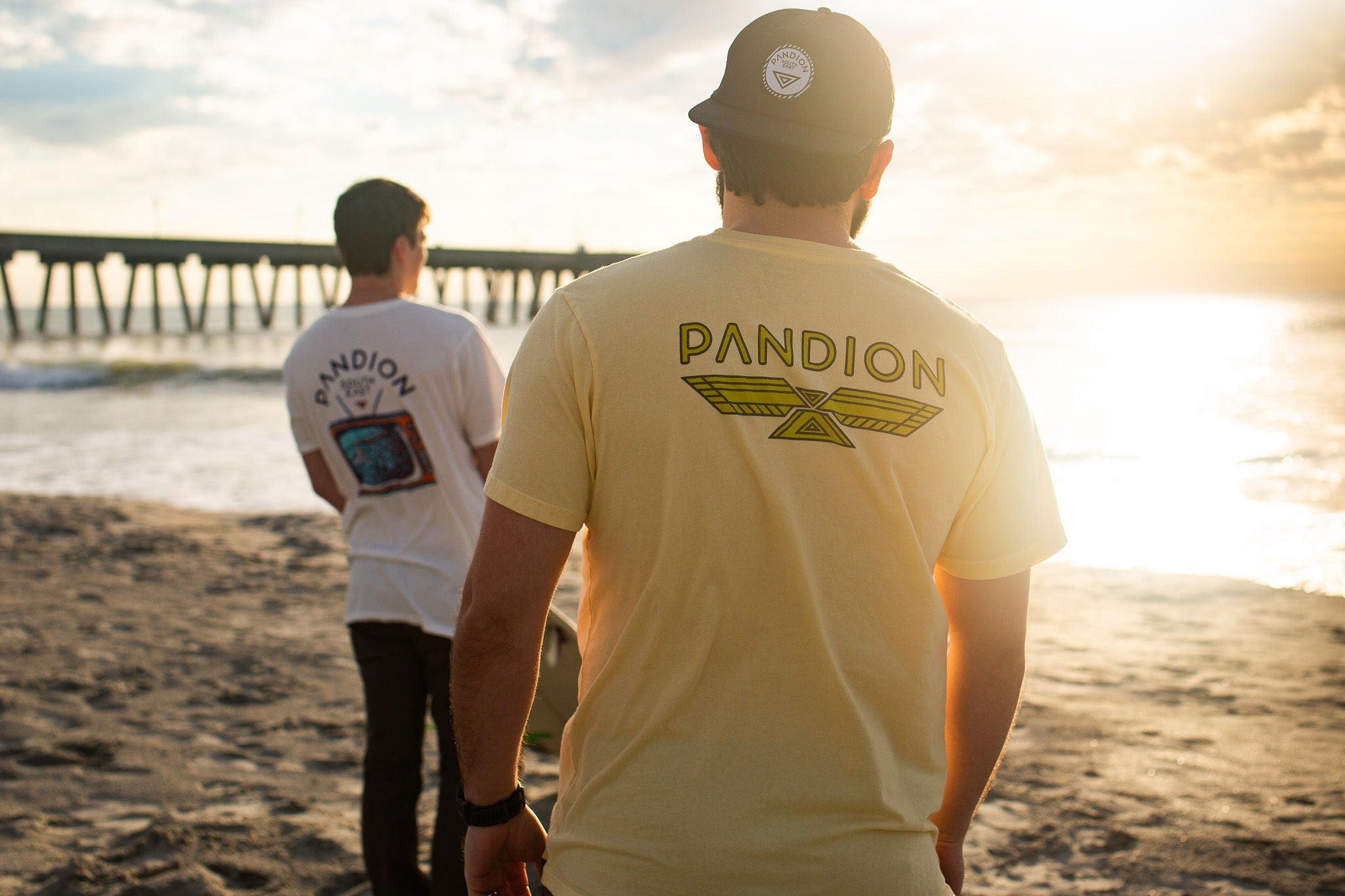 two guys on the beach watching the sunset wearing pandion southeast tee shirts